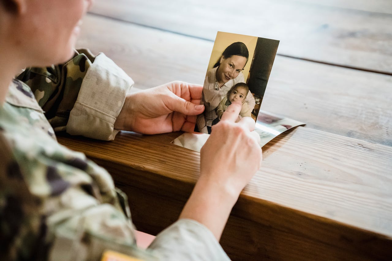 A soldier in uniform reminiscing while holding a photograph of family members.